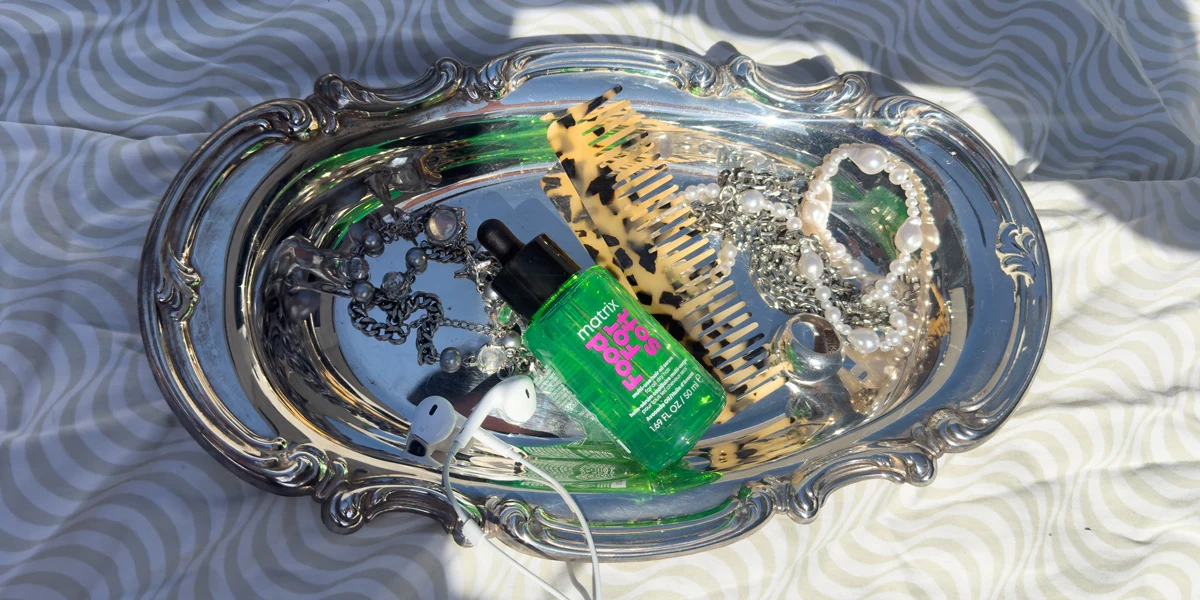A green Matrix hair serum bottle on a decorative silver tray with pearl and chain necklaces.