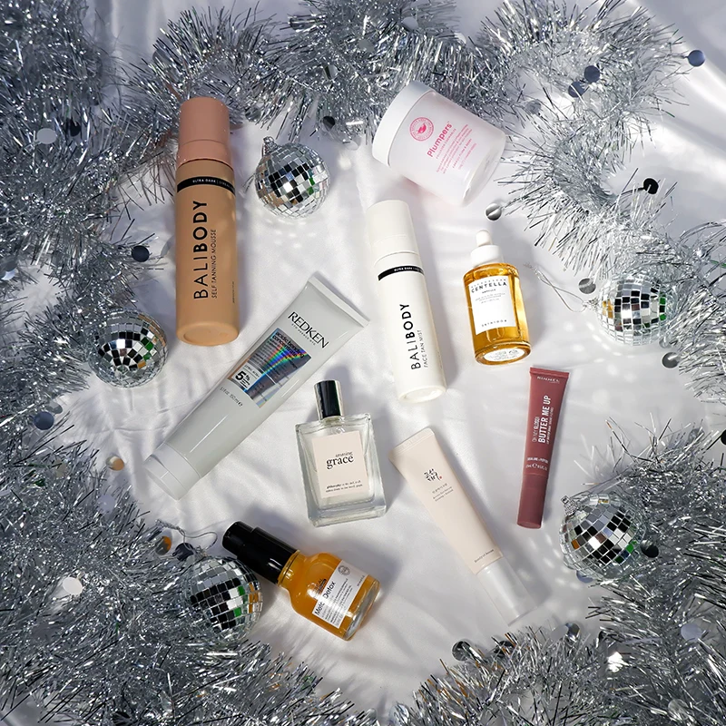 Beauty and skincare products arranged with silver tinsel garland and disco ball ornaments on white background in festive holiday layout.