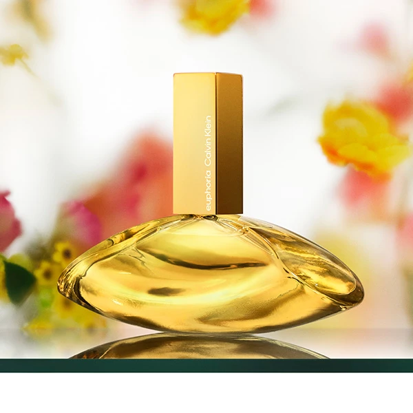 Calvin Klein Euphoria gold perfume bottle with mangoes, white and yellow orchids on a golden background.
