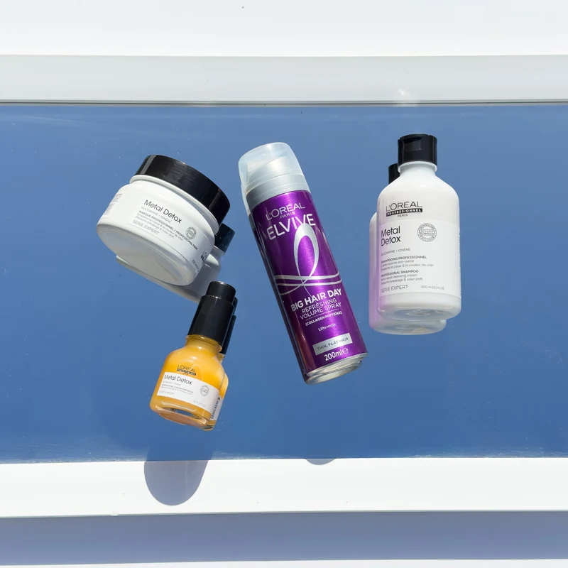 Four L'Oreal hair products on a blue surface: Metal Detox mask, serum, shampoo, and Elvive Big Hair Day volume spray.