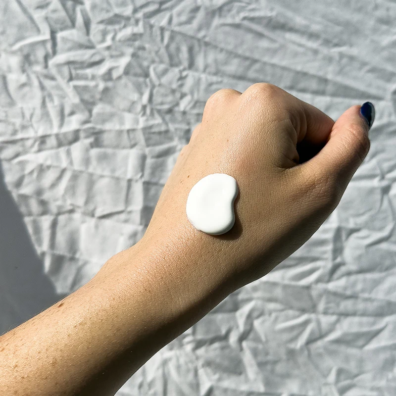 White moisturizing cream or lotion dollop on person's hand against crumpled white paper background.