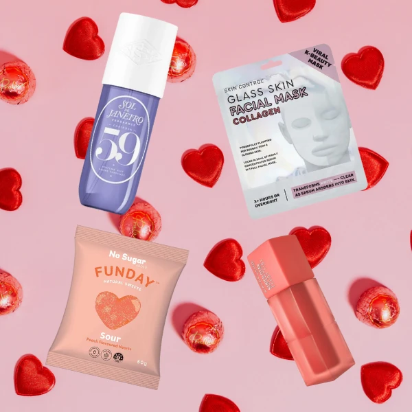 Beauty and wellness products including facial mask, serum bottle, and candy packaging scattered among red heart-shaped chocolates on pink background
