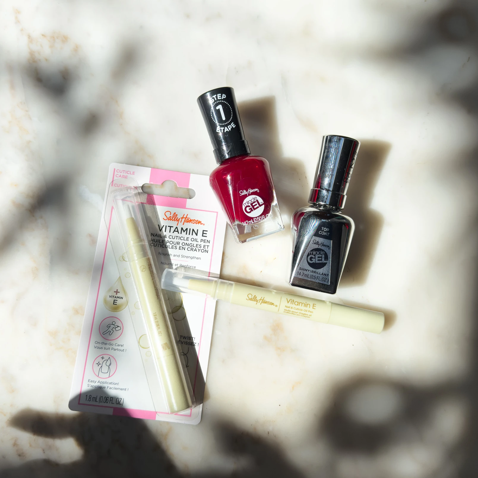 Collection of Sally Hansen nail care products including Vitamin E cuticle oil and gel nail polishes on a marble surface