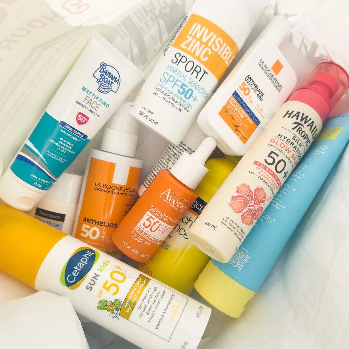 Various SPF 50+ sunscreen products including Cetaphil, La Roche-Posay, Hawaiian Tropic, and Avene arranged on a white surface.