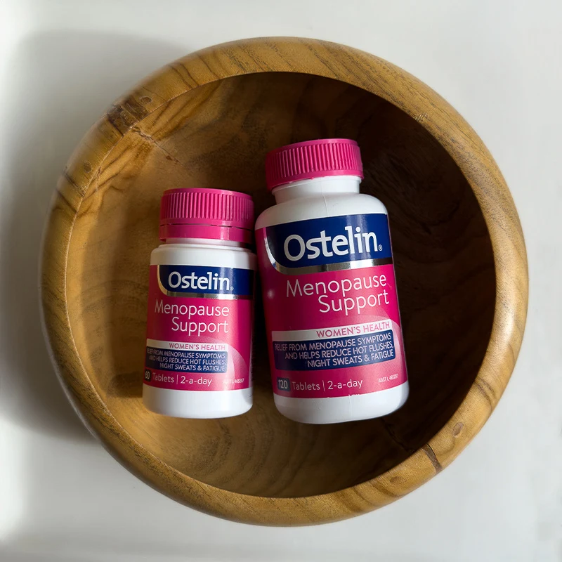 Two bottles of Ostelin Menopause Support supplements in a wooden bowl viewed from above.