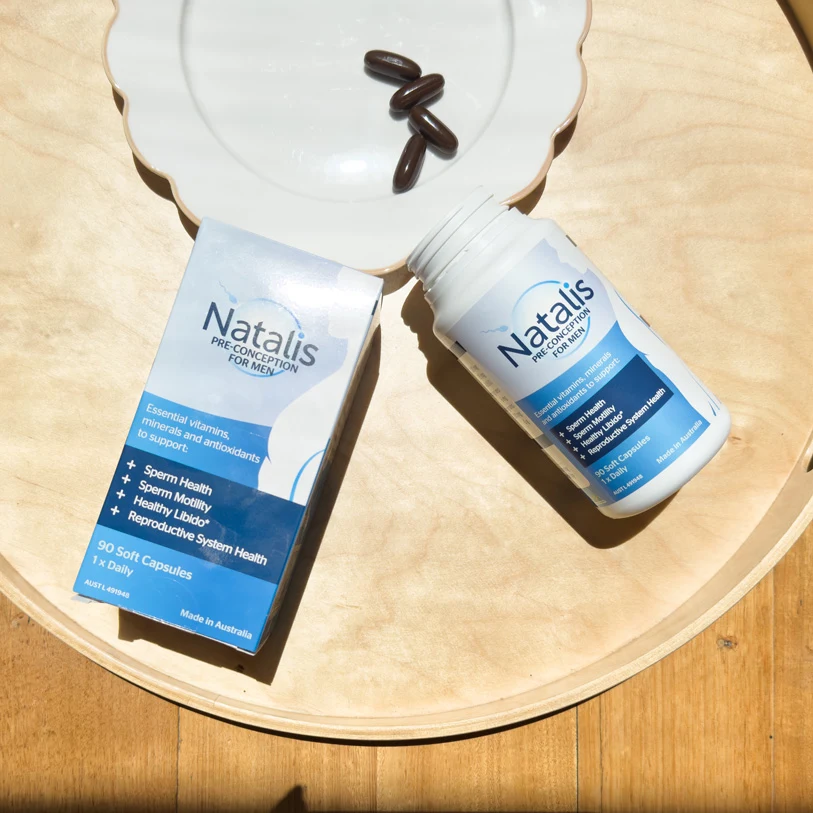 Two bottles of Natalis men's preconception supplements with soft capsules on a light wooden surface