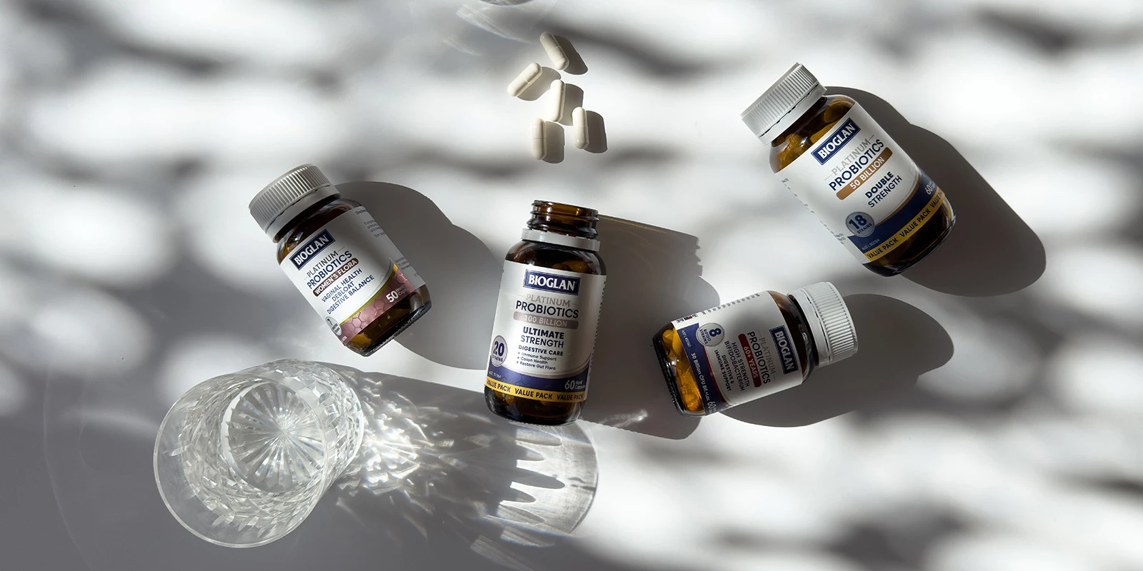 Multiple Bioglan probiotic supplement bottles arranged diagonally casting dramatic shadows on white background