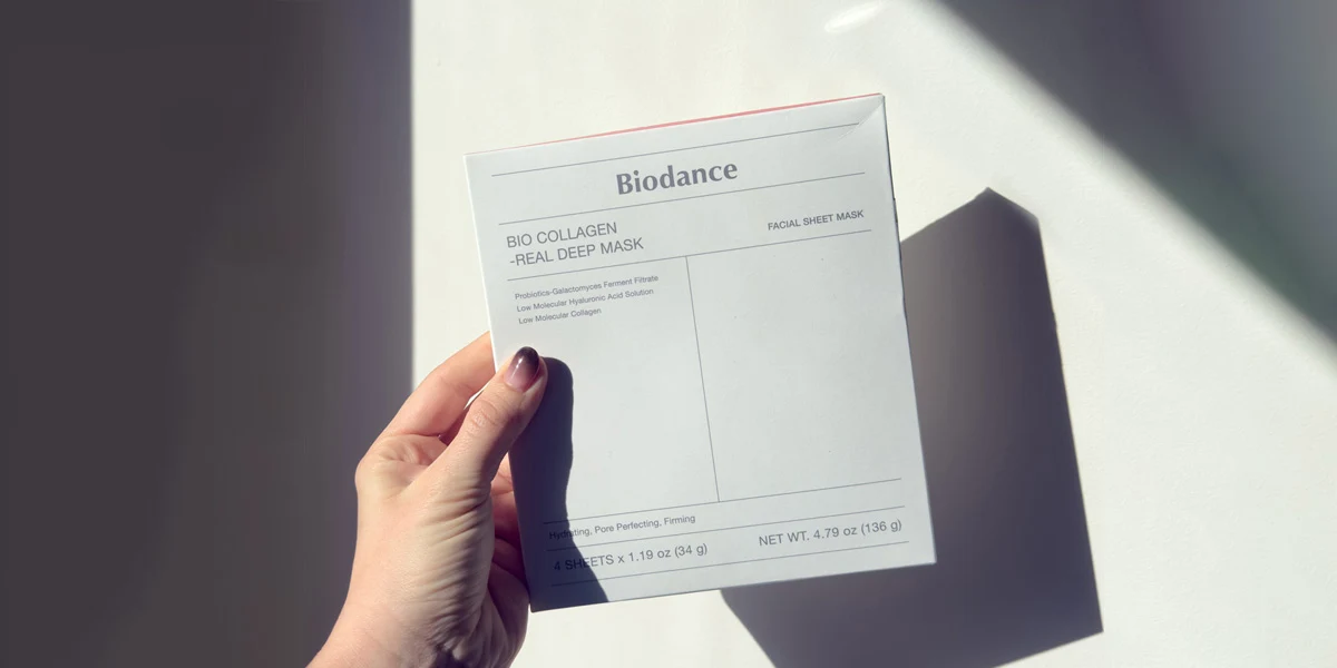 A hand holding a white box of Biodance Bio Collagen Real Deep Mask facial sheet masks in bright sunlight.