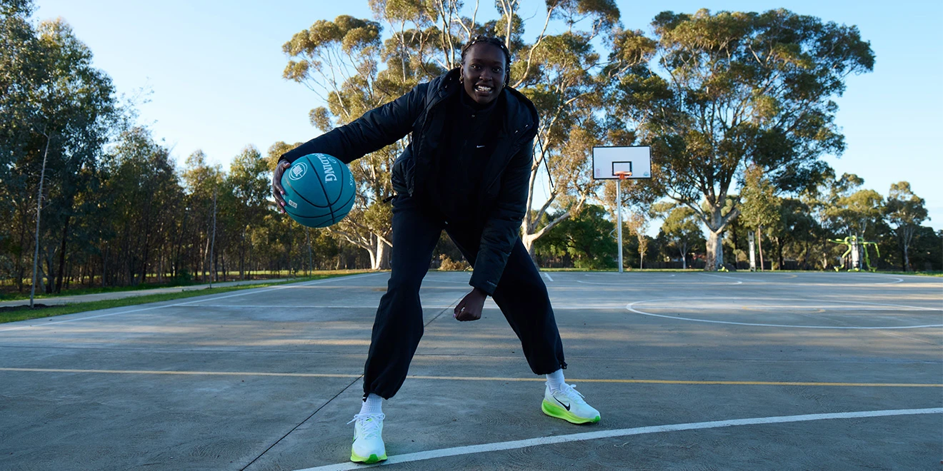 Basketball player in black athletic wear performs dribbling moves on outdoor court surrounded by eucalyptus trees.