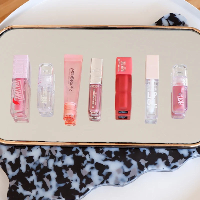 MCoBeauty lip products in pink and nude shades displayed on reflective surface with black and white patterned edge.