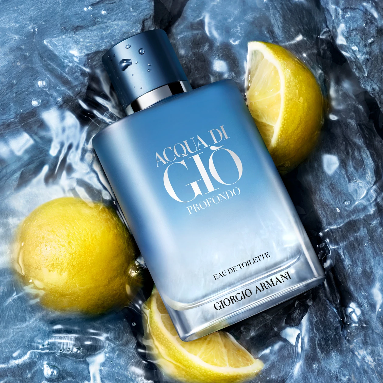 Blue Acqua di Gio perfume bottle lying on ice with fresh lemon slices, creating a cool and refreshing composition