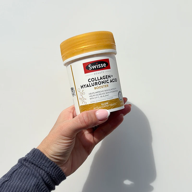 Hand holding Swisse Collagen and Hyaluronic Acid supplement bottle with gold cap against white background