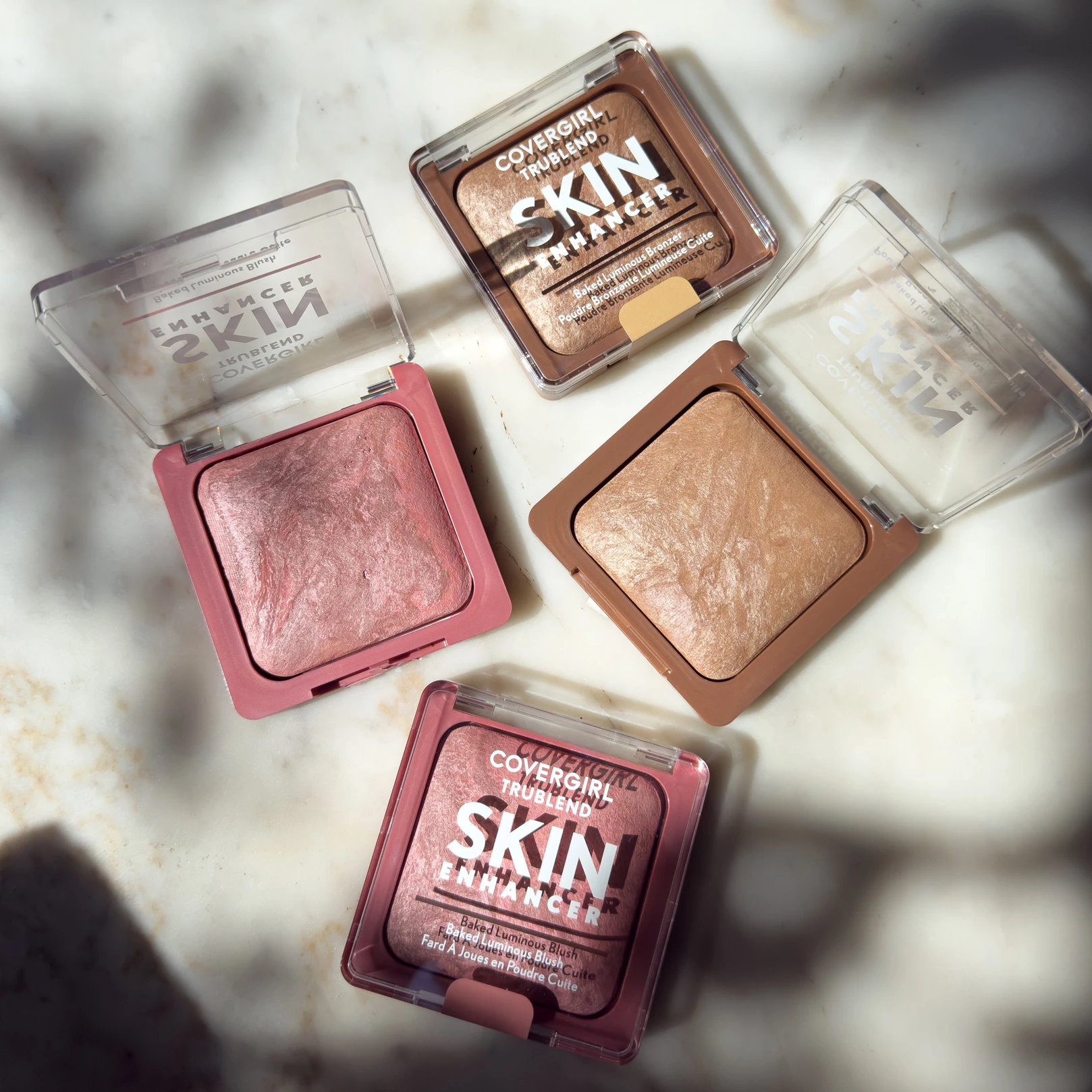 Covergirl Skin Enhancer makeup compacts in various shades of pink and bronze, arranged on a light marble surface