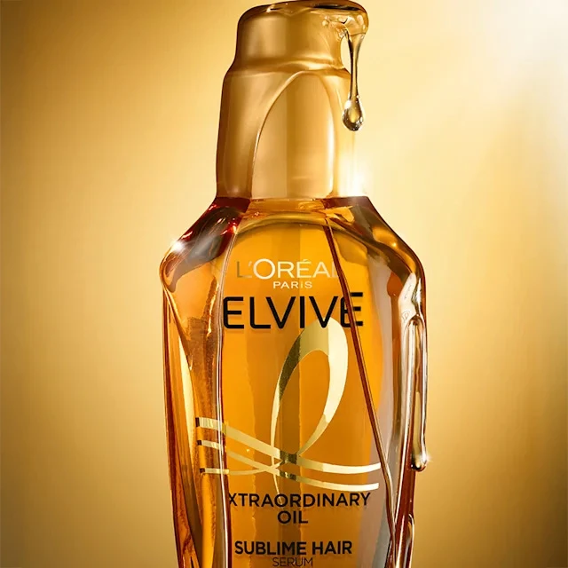 Glass bottle of L'Oreal Elvive Extraordinary Oil hair serum with golden liquid against warm-toned background.