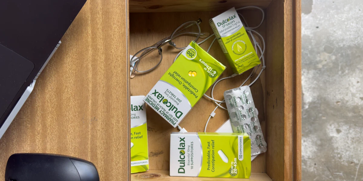 A wooden drawer containing multiple Dulcolax product boxes, glasses, a charging cable, and blister packs of tablets.