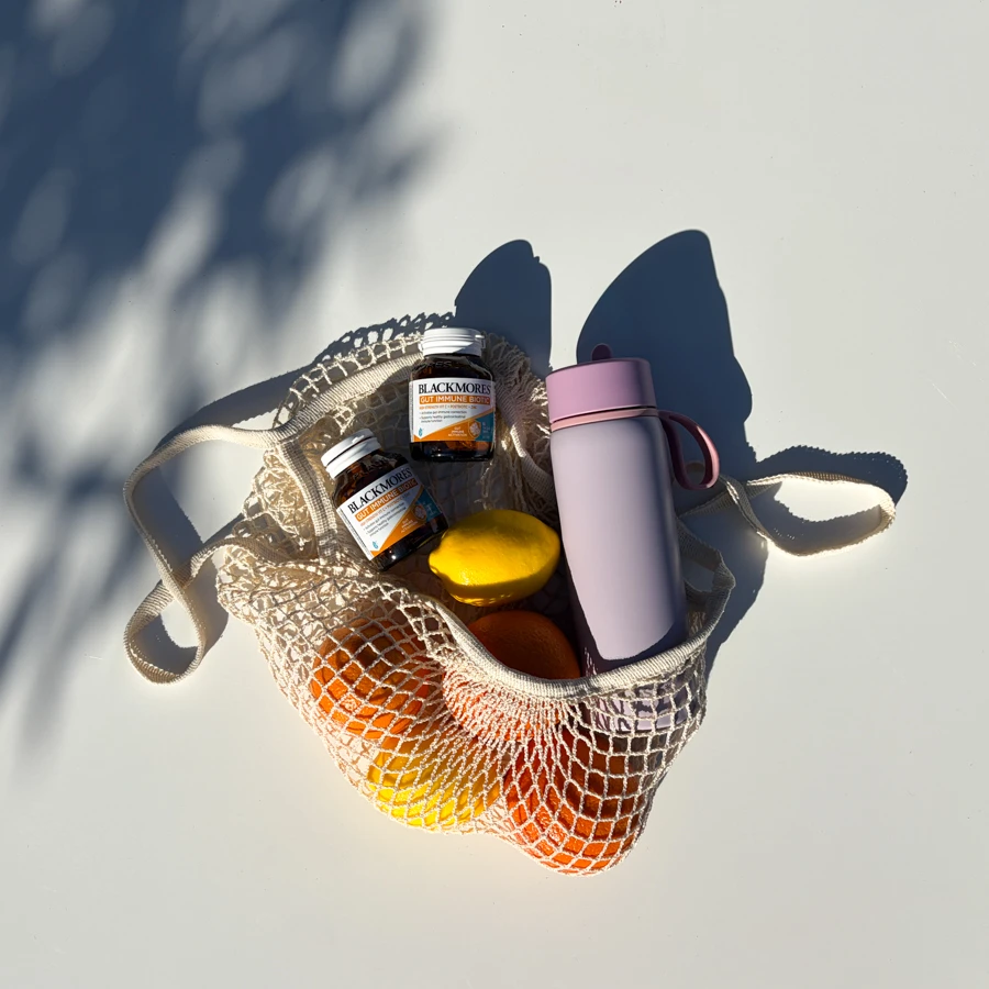 Two Blackmores Gut Immune Biotic supplement bottles on a white tray with orange slices and tablets in natural sunlight.