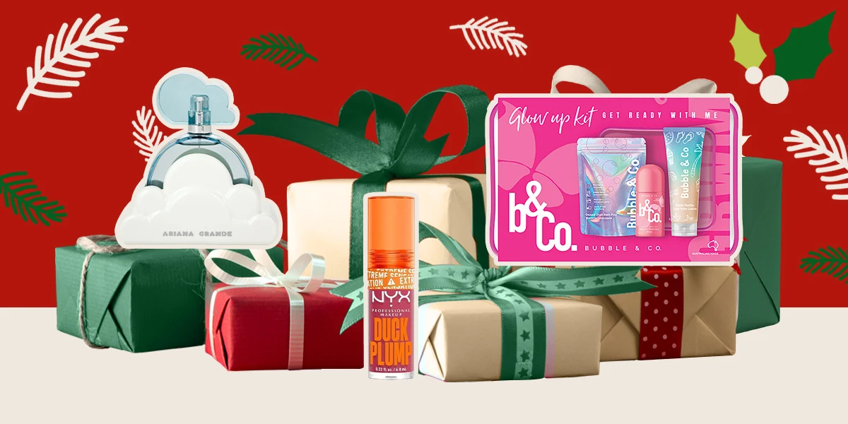 Holiday gift display featuring perfume, beauty products, and wrapped presents against a festive red background with holly leaves