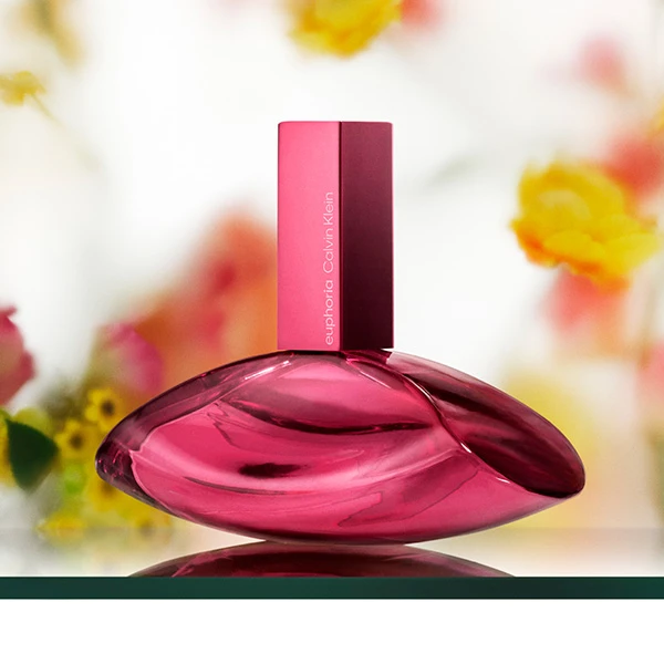 Calvin Klein Euphoria perfume bottle in deep pink, surrounded by orchids and vanilla pods on a pink background.
