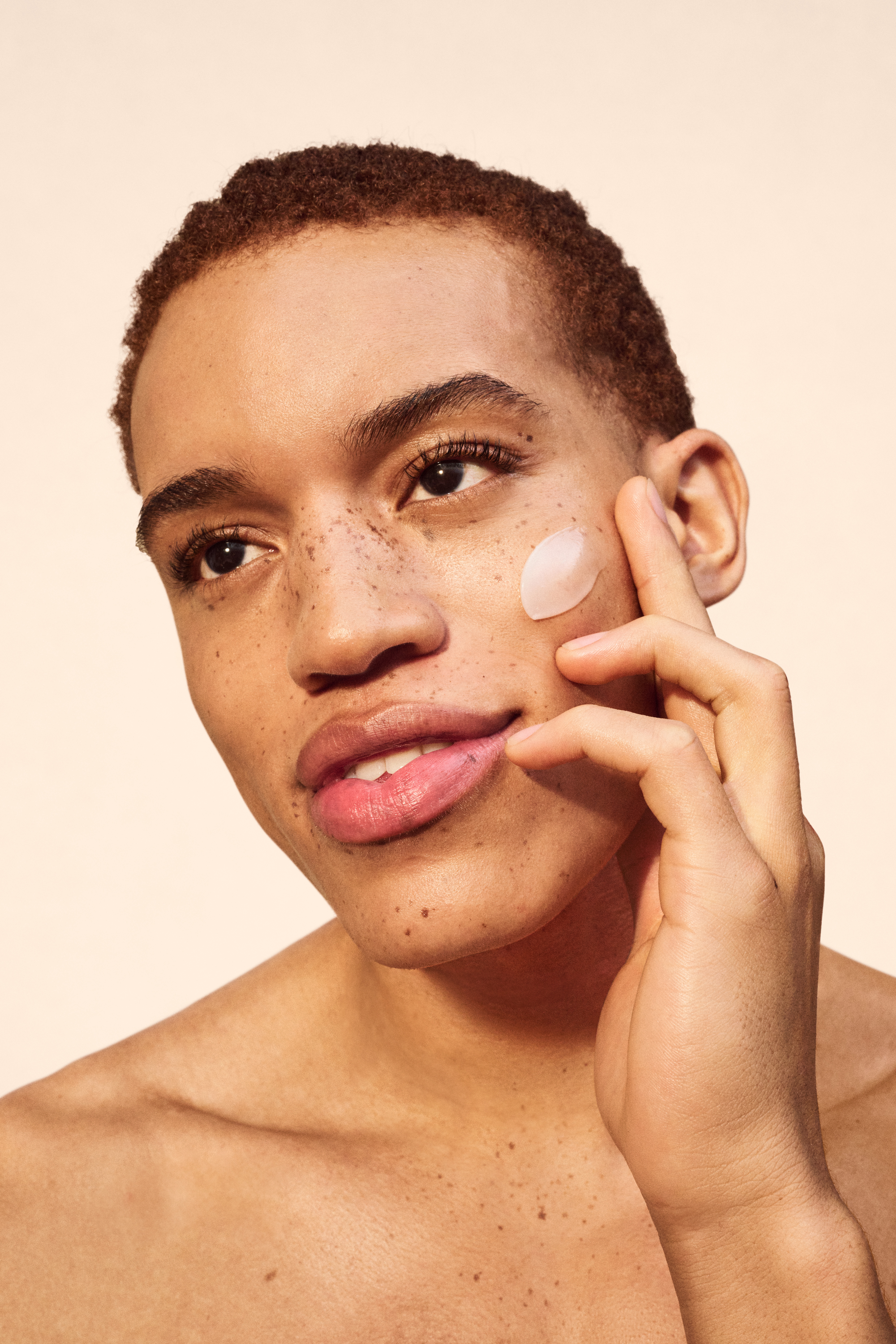 woman rubbing emollient cream into her shoulder with blue back background and oat imagery to the left
