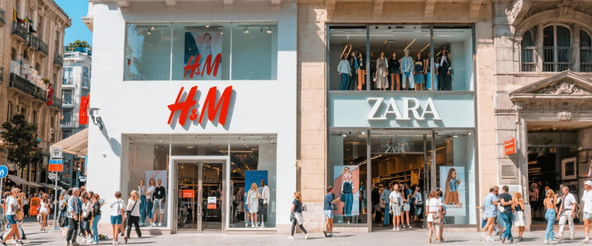 H&M- og Zara-butikker ved siden av hverandre, solfylt travel gate.