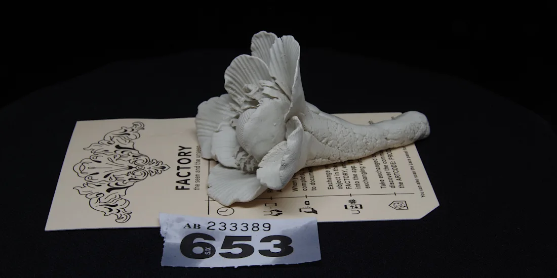 A small ceramic flower overlaying a paper with text about it and a raffle ticket numbered 653
