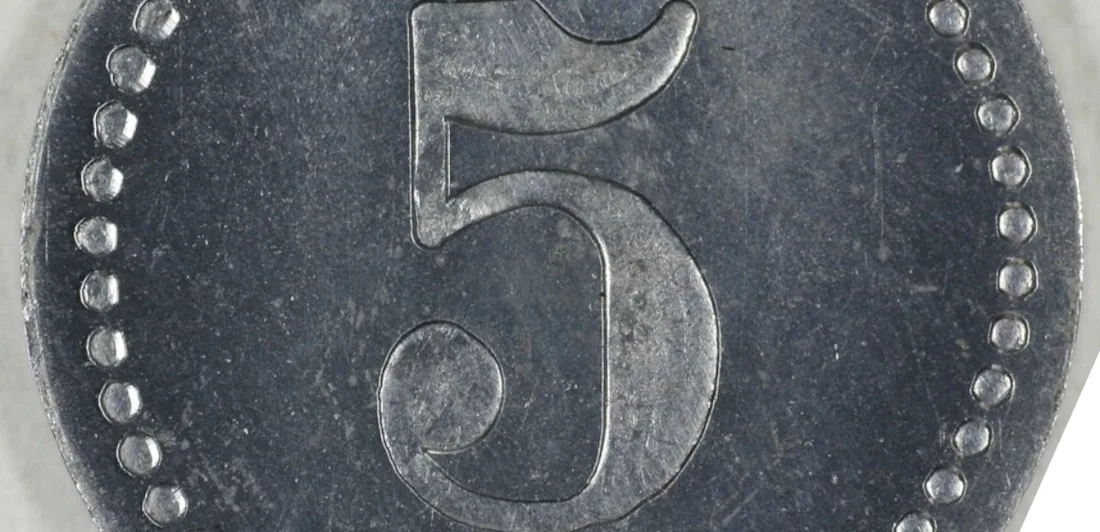 A close-up of a metal coin with the number 5 embossed in the center. The edge of the coin is decorated with a dotted border. The surface shows signs of wear and age.