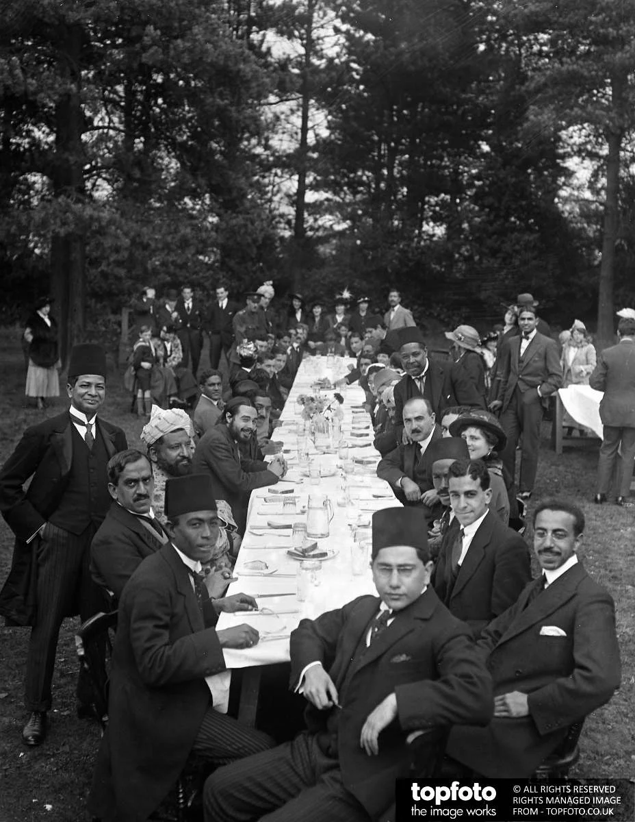 black and white photograph, a group of people sit and stand around a long table