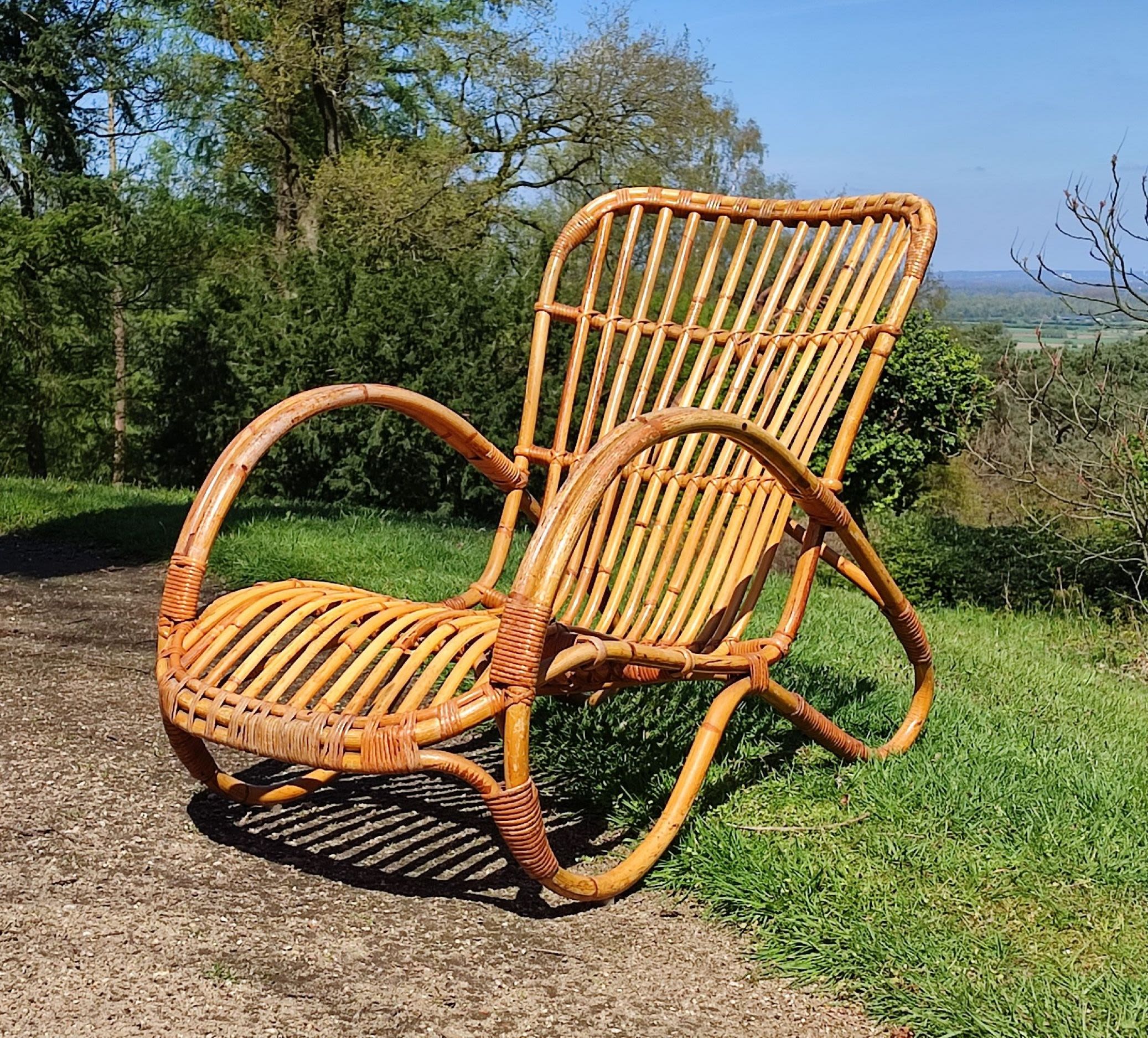 a rotan lying chair made from curved pieces of wicker on a grass patio.