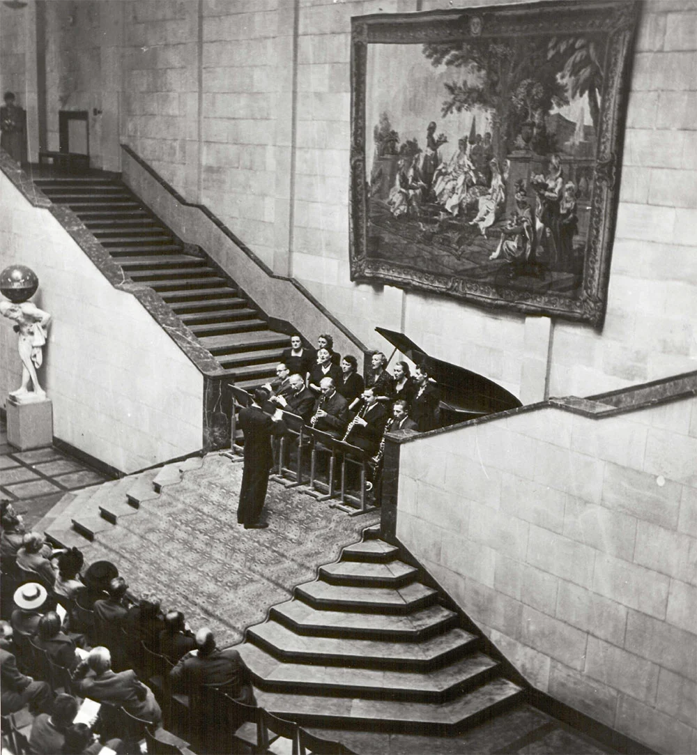 black and white photograph, a concert with conductor in a museum photographed from above