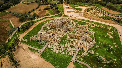 Aerial view of an ancient stone ruins complex surrounded by green grass and paths in a rural landscape.