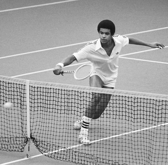 Photographie en noir et blanc d'un jeune Yannick Noah en action sur un court de tennis.