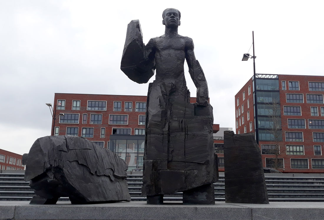 Une grande statue en bronze d'Anton de Kom sur une place d'Amsterdam qui porte son nom.