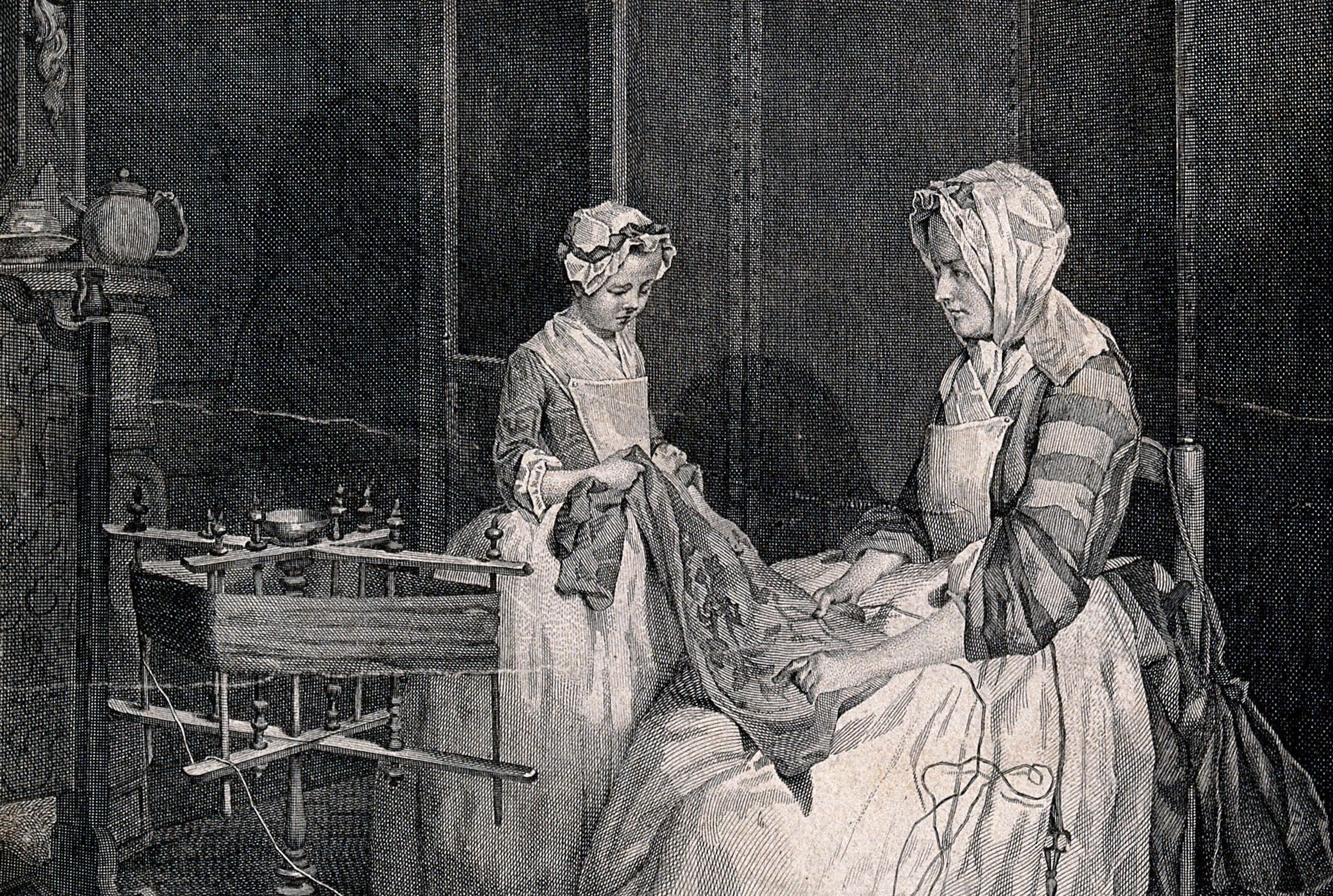 A mother and daughter are working together on a piece of cloth, a spinning wheel sits nearby