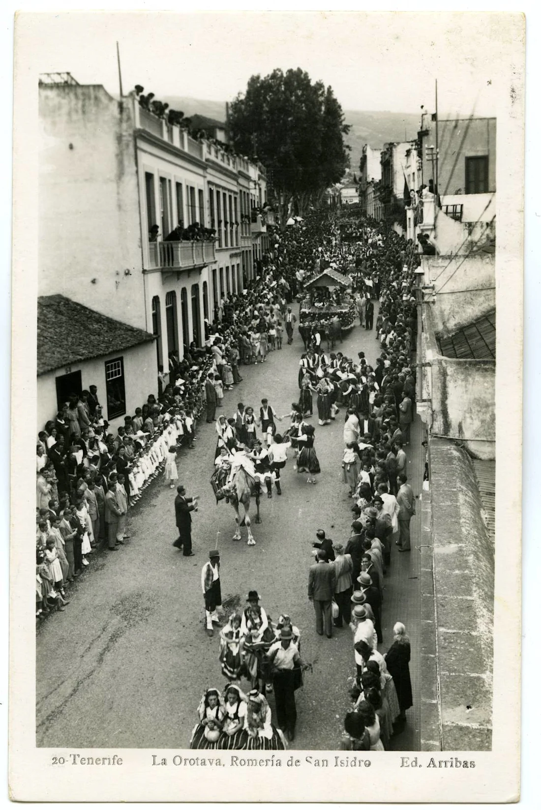 fotografía en blanco y negro, gente haciendo una procesión en una calle con otros mirando desde los lados.