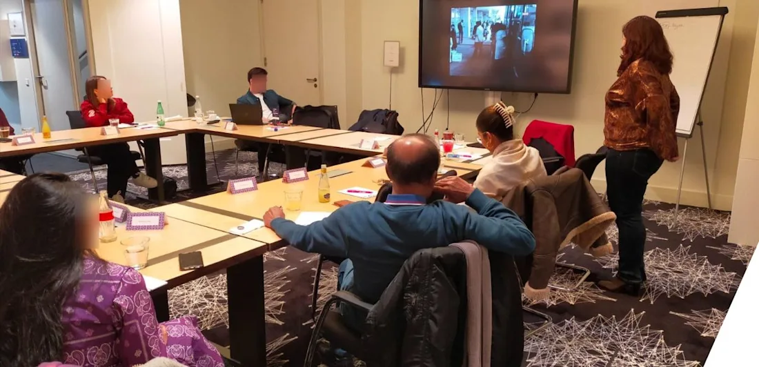 Participants sat around tables, looking at a screen, in a workshop