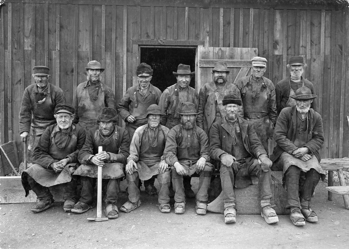 black and white photograph of a group of old men sitting posing in front of a mine building