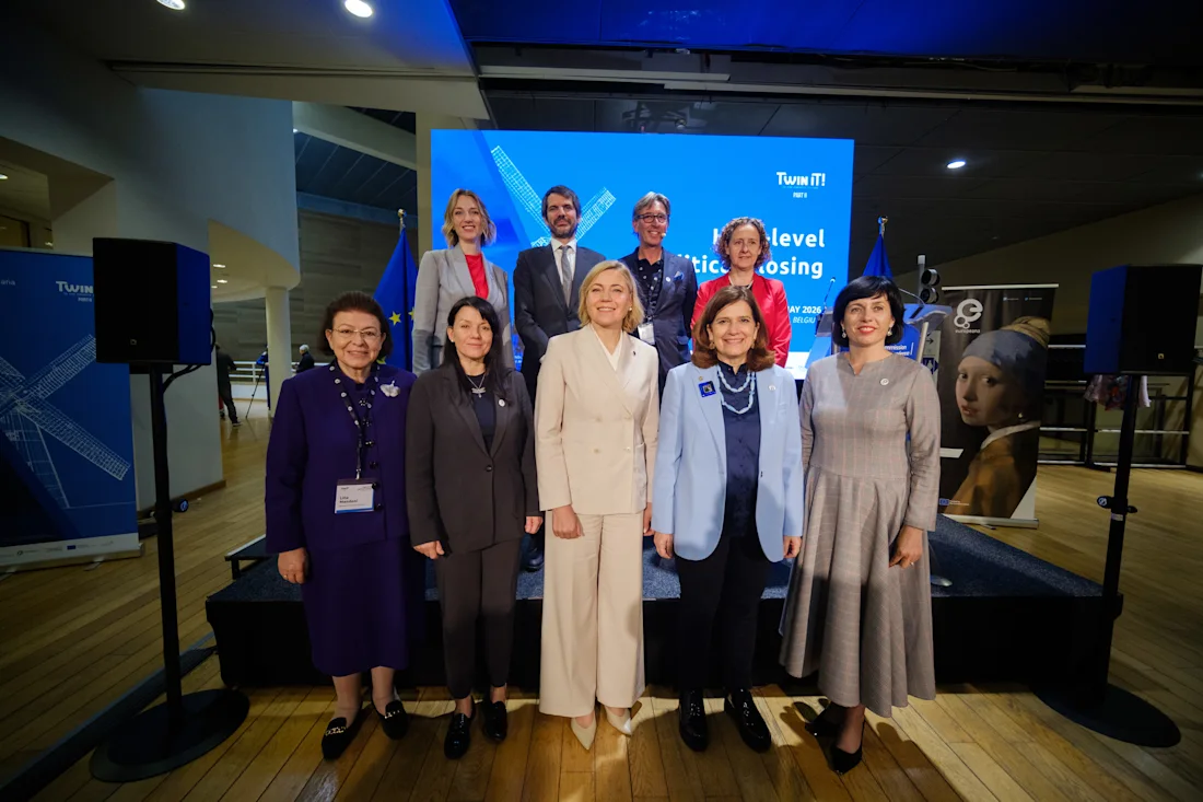 Nine honoured dignitaries stand on a stage in front of a blue backdrop with microphones and banners.