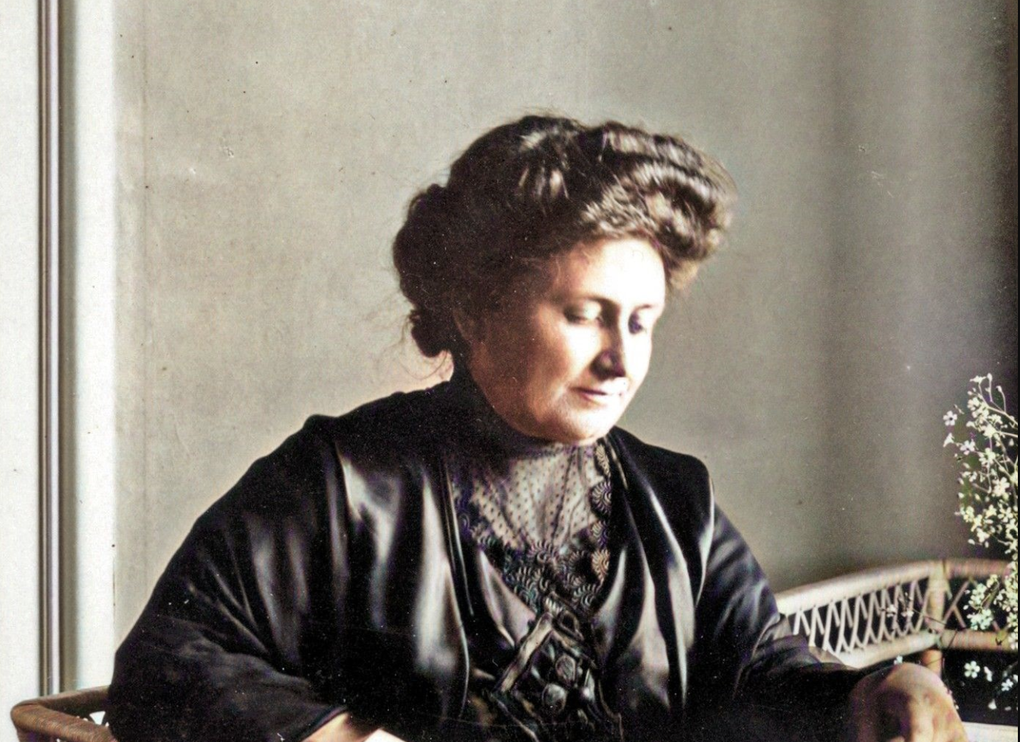 Maria Montessori in a black dress, hair pinned up, looking down at a book she is reading. 