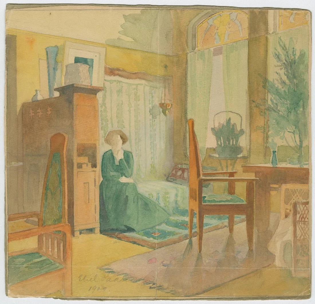 A woman in a green dress sits in a sunlit, softly colored living room with wooden furniture and large windows.
