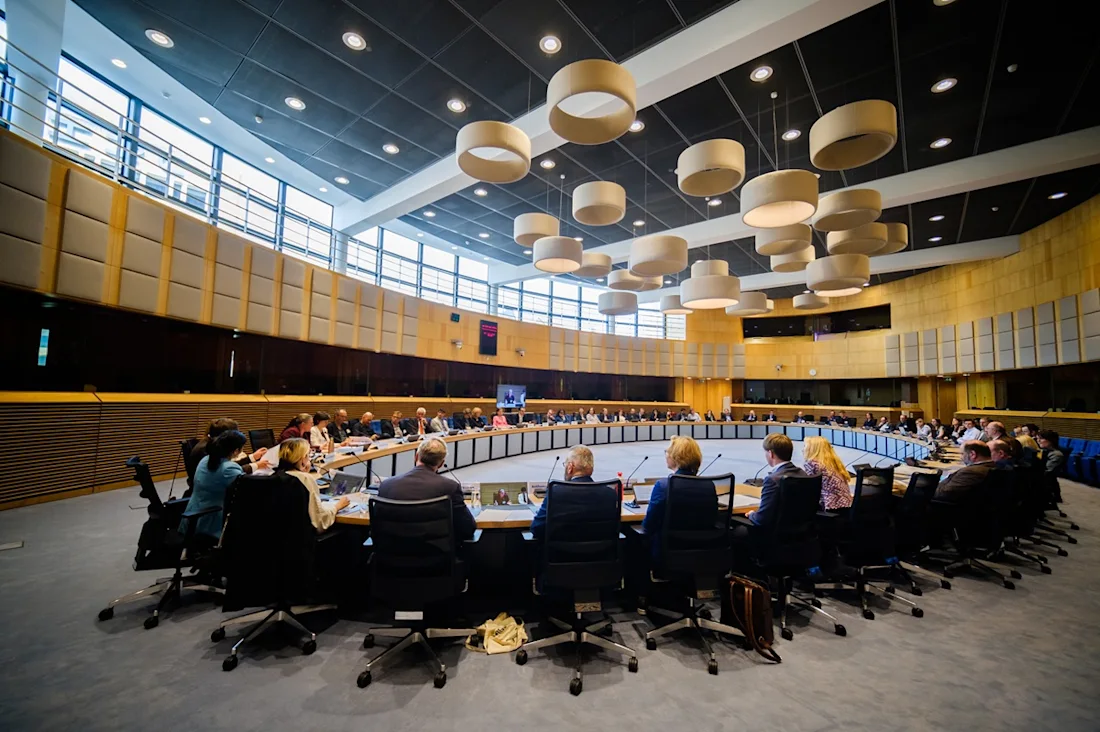 Participants at the High-level event of the Twin it! 3D for Europe s culture campaign are seated around a large curved table, in a modern, paneled room with large lamps hanging from the ceiling