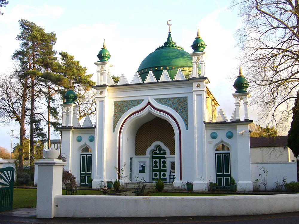 colour photograph of a white mosque building with a mosaic panel and green domes