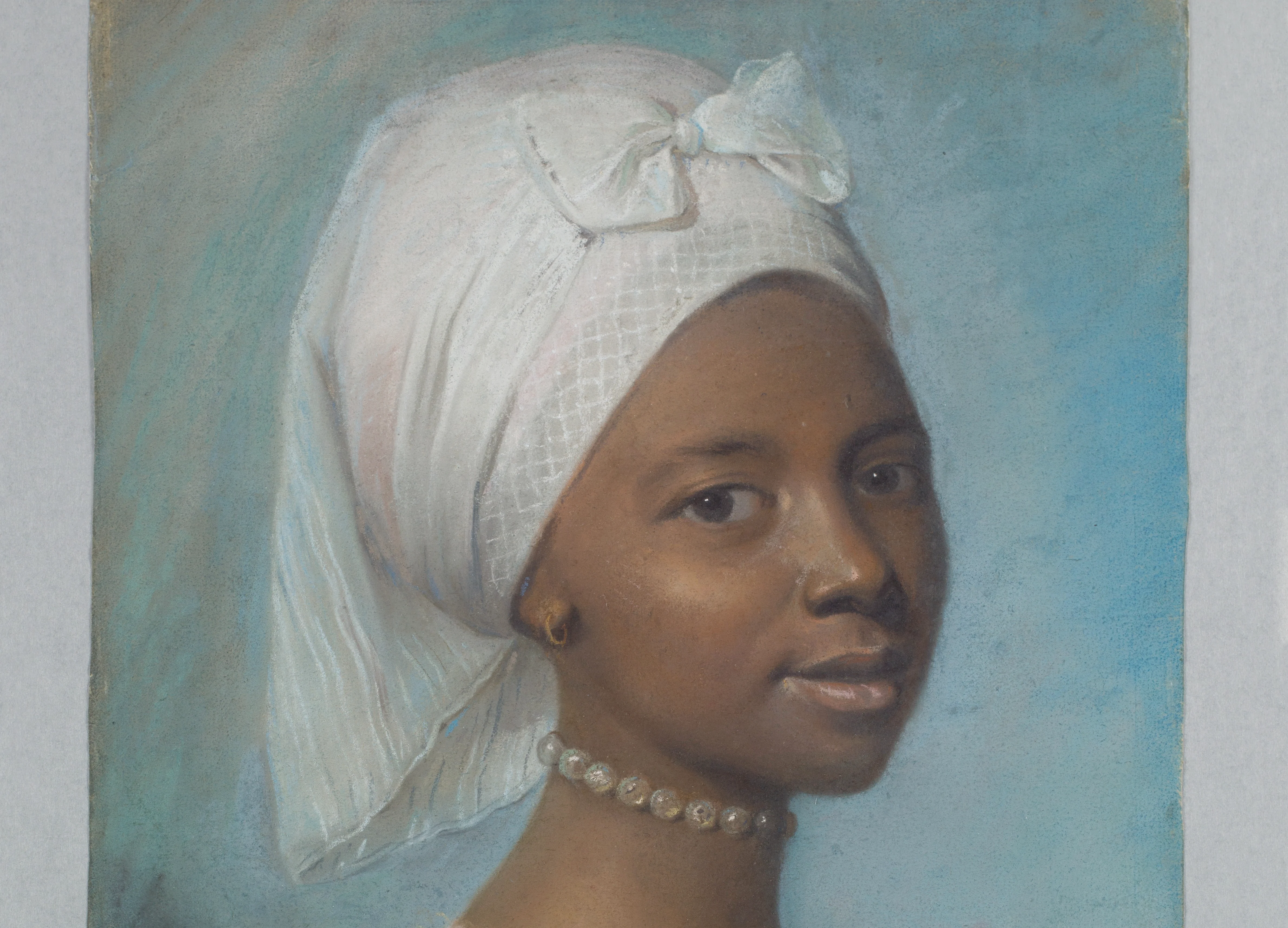 Portrait of a woman with a white headscarf, pearl necklace, and blue background.