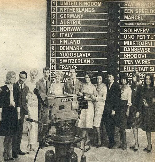 black and white photograph, a group of performers line up for a photograph under a large scoreboard.