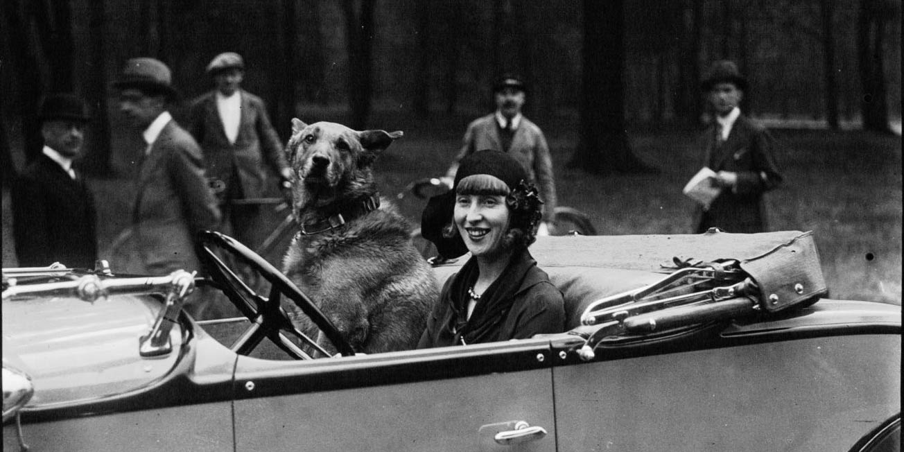 black and white photograph of Suzy Solidor who sits in a car with a large dog sitting next to her.