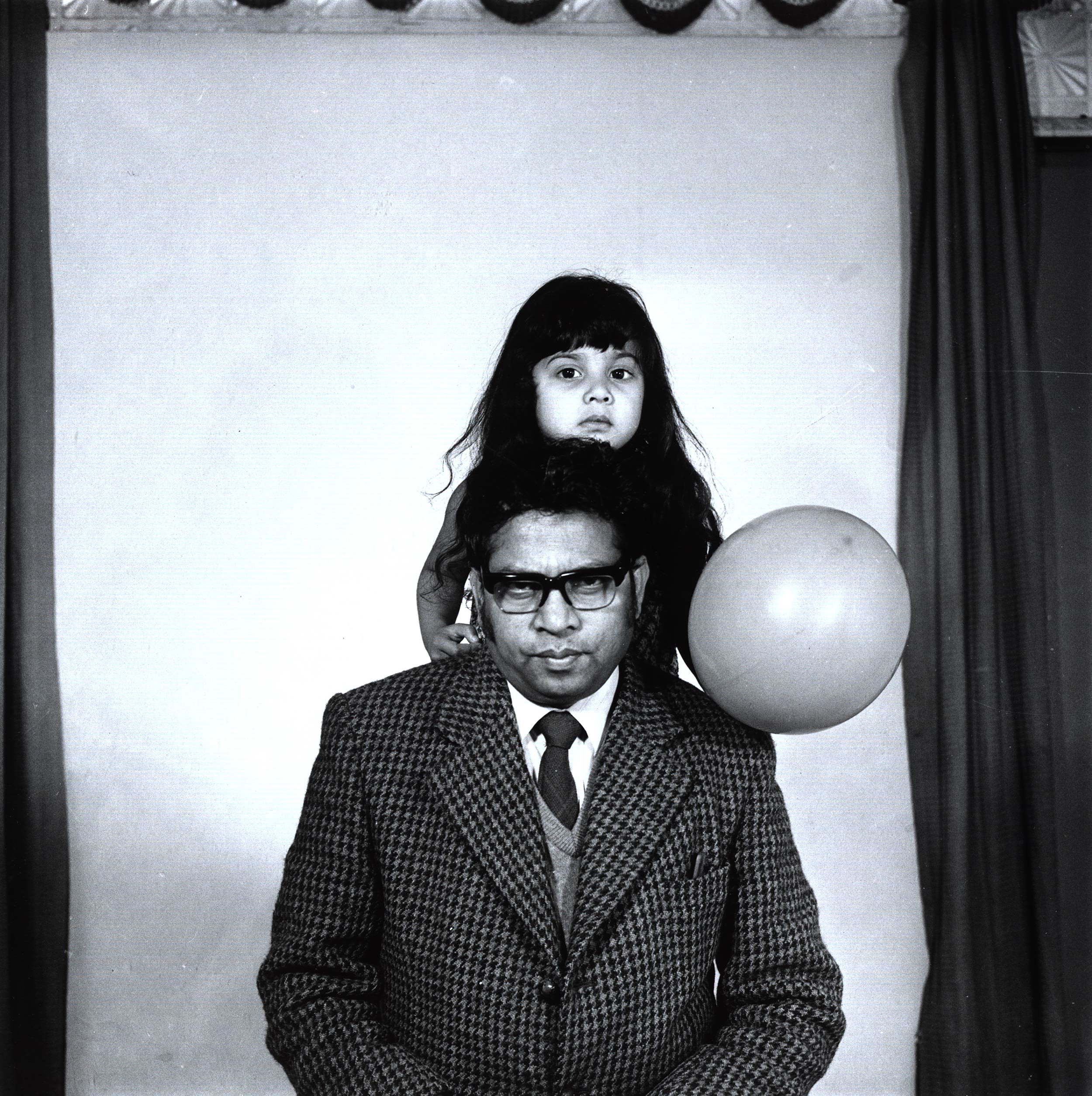 black and white photograph of a man wearing suit with a young girl holding a balloon standing behind him.