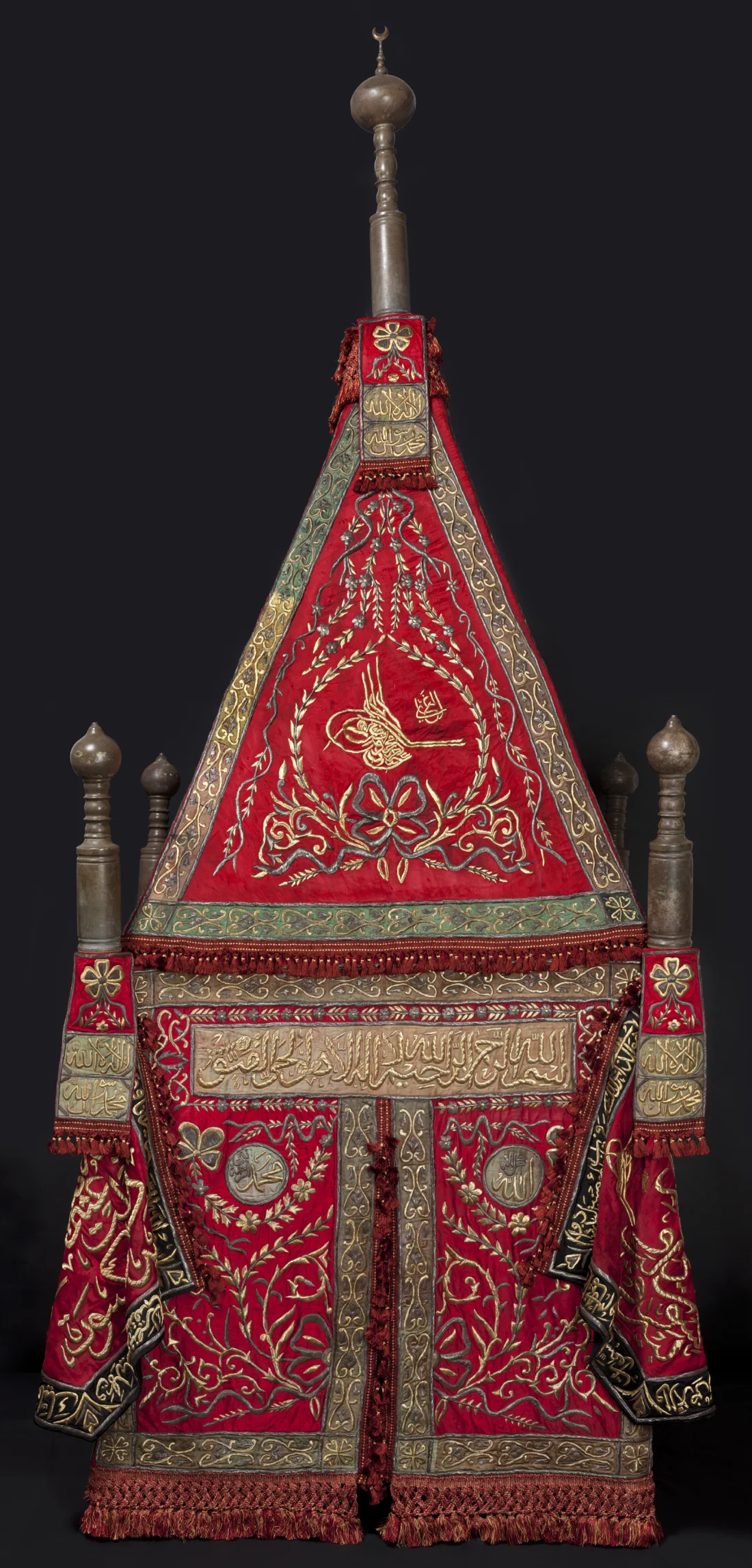 banners and finial banners of red silk, with green and gold-coloured silk appliqués, embroidered in silver and silver-gilt wire over cotton thread padding; finials of copper alloy; contemporary wooden frame