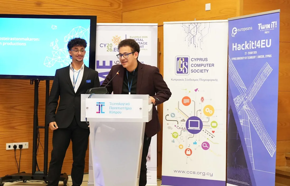 Two young men present at a podium during a tech event, with banners and a screen behind them.