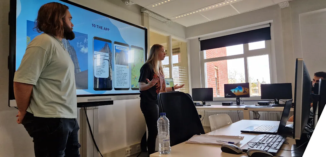 Two students present a project in front of a projected slide show