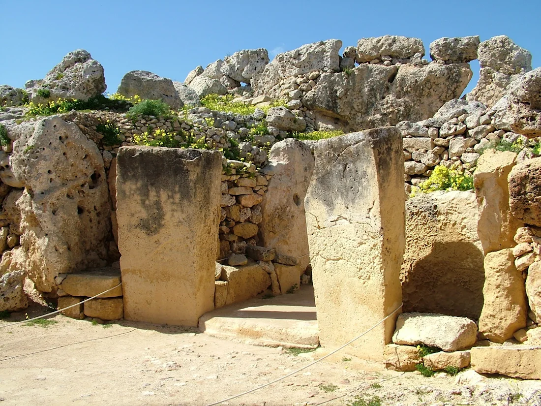 Ancient stone ruins with large upright slabs and rocky walls under a blue sky.