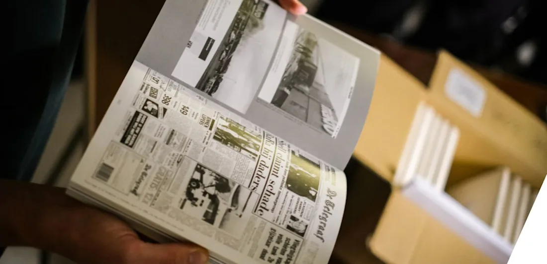 Hands holding open a book which shows newspapers and photographs in black and white